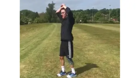 Tom Wilson Tom in a green field with his hands in the air, following a run uphill