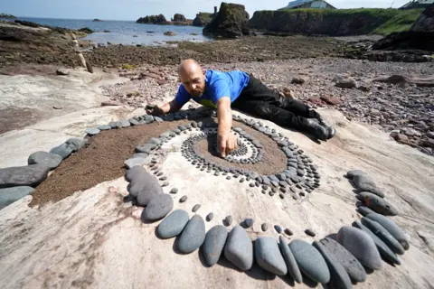 Andrew Milligan / PA Media Mark Antony Haden Ford works on an artwork at Eye Cave beach in Dunbar, Scotland, ahead of the European Stone Stacking Championships, on 8 July 2021