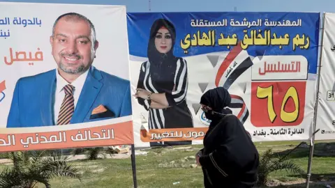 Reuters An Iraqi woman walks next to election campaign posters for candidates in Baghdad, Iraq (5 October 2021)