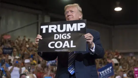 Getty Images US President Donald Trump holds up a "Trump Digs Coal" sign as he arrives to speak during a Make America Great Again Rally at Big Sandy Superstore Arena in Huntington, West Virginia, August 3, 2017