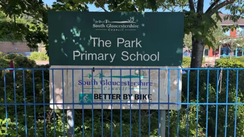 BBC A sign for the Park Primary School, with white letters on a green background, behind a thin blue metal railing fence