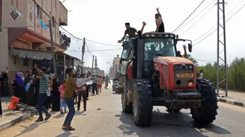 SAID KHATIB / AFP Palestinians drive an Israeli tractor that was seized after crossing the border fence with Israel from Khan Yunis in the southern Gaza Strip on October 7, 2023.