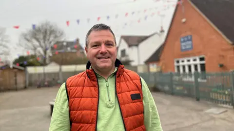 Kerrin is wearing a green long sleeve with orange padded vest behind the school