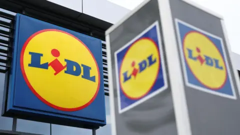Reuters The outside of a Lidl supermarket, which has the Lidl logo clearly in vision. The logo has the brand name written in the middle in blue and red, and it is surrounded by a yellow circle with a red boundary.