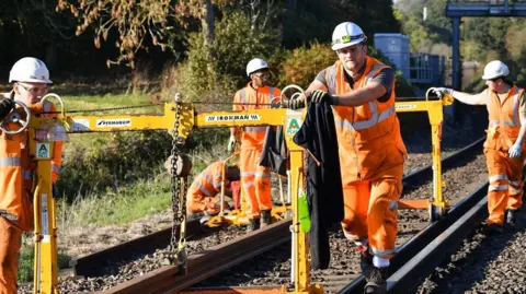 Five contractors wearing orange hi-vis clothing carrying out maintenance work on a railway line.