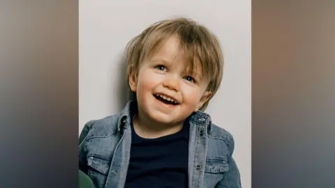 Little boy in denim jacket smiles at camera