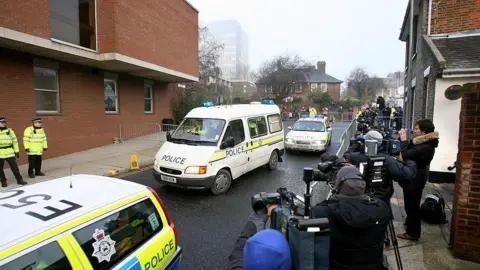 Getty Images A police van carrying Steve Wright arrives at Ipswich Magistrates' Court. A police car is in front of the van, with another behind. A large media pack are situated behind metal barriers with many cameras pointing towards the road. 