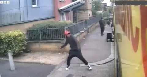 A man throws a stone at the side window of an ambulance parked on a suburban street