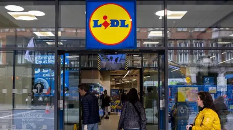 A red, blue, and yellow Lidl sign above a Lidl supermarket with shoppers entering.
