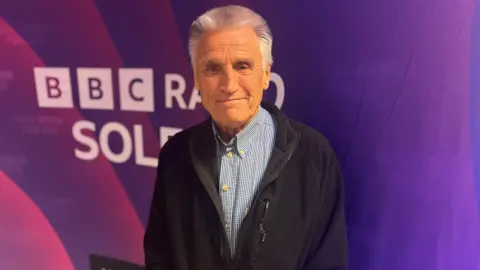 Bob Lakin a grey haired man stood in front of a purple BBC Radio Solent backdrop