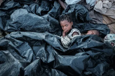Yasuyoshi Chiba / AFP Enia Joaquin Luis, 11, wakes up beside her sister Luisa, 6, under plastic sheets to protect themselves from rain at a shelter in Buzi, Mozambique, following Cyclone Idai in March.