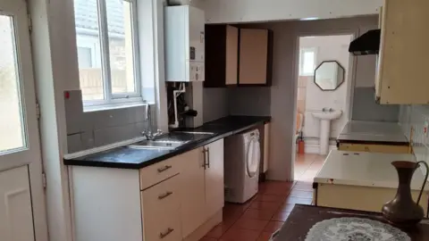 A galley kitchen with a door to the left leading to the garden and a loo in the back of the house.