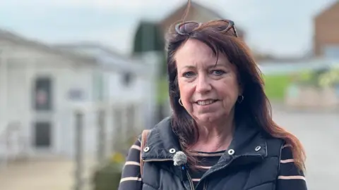 Helena Davison is wearing a black giley over a black and beige striped top and has tortoiseshell sunglasses in her hair.