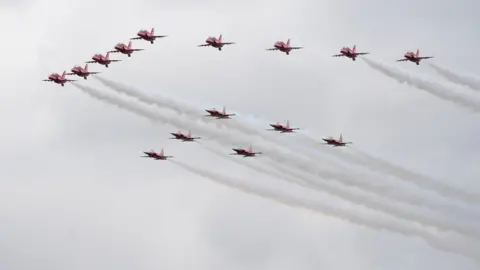 PA Media Aircraft are seen in the sky during a flight display. The aircraft are red, with white condensation trails.