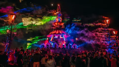 Chris Cooper A tall neon structure surrounded by people at night as it lights up the sky