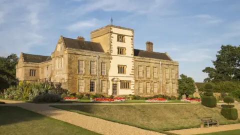 James Dobson/National Trust The frontage of a three-storey stately home, Canons Ashby, in the midst of lots of shrubs and plants