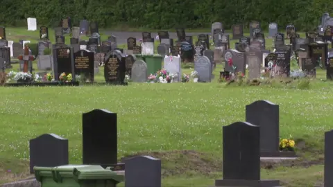 BBC Rows of gravestones in Rawtenstall Cemetery. Many of the graves are adorned with flowers.