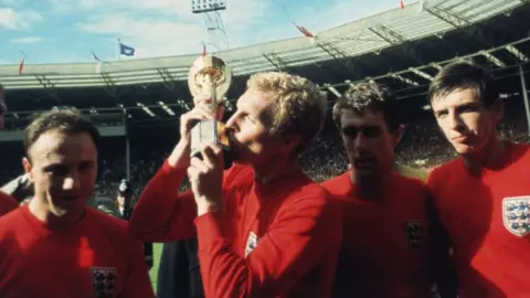 England captain Bobby Moore kissing the Jules Rimet trophy as the team celebrate winning the 1966 World Cup final