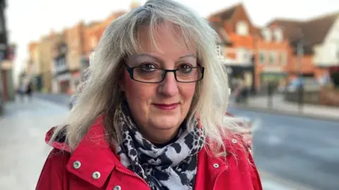 Stuart Woodward/BBC A blonde woman smiling. She is wearing glasses and a red coat