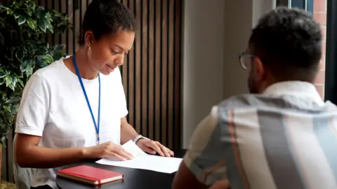 Getty Images A young woman in a modern office at a table with a co-worker