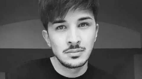 Family photograph A black and white image of the late Martyn Hett who had dark brown hair and stubble and was wearing a black crew neck top.