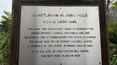 Paul O'Gorman/BBC Chatterton Playing Field Peace Memorial plaque inscribed in metal in front of some trees.
