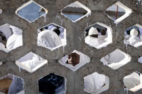 PATRICK MEINHARDT / AFP A young follower looks inquisitively through an opening in the brise-soleil wall.