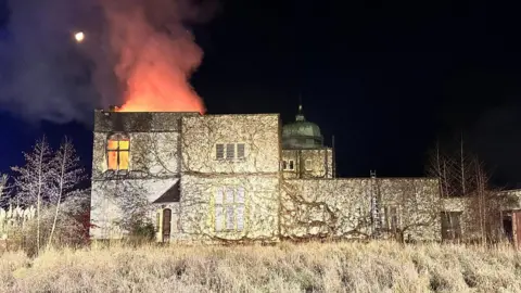 The fire at Bignell House during the night. Smoke and flames are seen coming from the roof.
