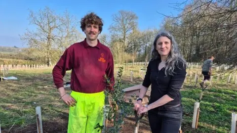 Swindon Borough Council Two people stand together in a field of young trees being planted. 