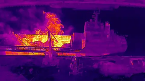 Humberside Fire and Rescue Service An aerial image of a cargo ship with a major fire burning in a hold taken on a thermal camera. It is a purple image with a large orange and yellow heat spot in the centre.