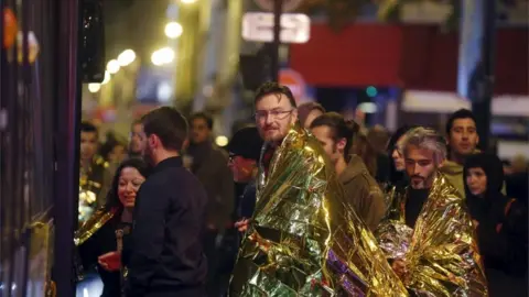 Reuters People warm up under protective thermal blankets as they prepare to board a bus to be evacuated near the Bataclan concert hall following fatal attacks in Paris, France, 14 November2015
