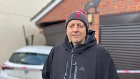 An image of Andrew Brown wearing a Liverpool FC bobble hat and black coat