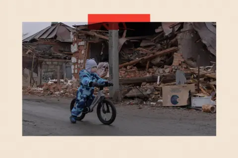 Gwara Media/Global Images Ukraine via Getty Images A child rides a bicycle near destroyed houses in Zolochiv, Kharkiv Oblast, Ukraine