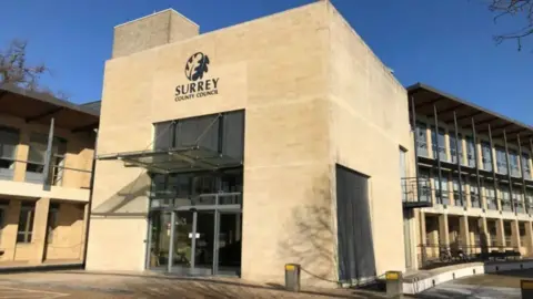 Local Democracy Reporting Service A grey stone building. The building has a glass awning in front of it with a sign above it. The sign reads: "Surrey County Council".