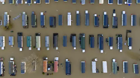 PA Media A drone image taken at Billing Aquadrome, looking directly down from height on about 60 caravans - all of which are surrounded by the same brown floodwater.