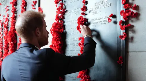 PA Media Prince Harry is pictured in a dark suit reaching out to place a poppy on a memorial wall commemorating Australian war dead from the Afghanistan conflict