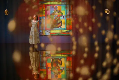 EPA A woman standing next to a large colourful painting, with translucent beads in the foreground in Zadie Xa's installation