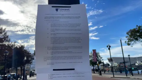 The Public Space Protection Order notice strapped to a lamppost. In the background is the Liverpool docks.