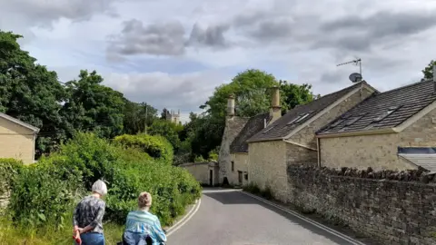 billyboy WEDNESDAY - A narrow street with double-yellow lines at either side, lined by stone walls and homes on the right side and green bushes on the left. Taken inNorth Hinksey