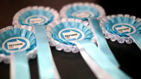 A close-up of five Reform UK election rosettes in turquoise blue and white colours.