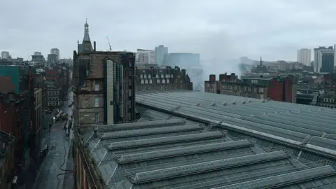 Getty Images An aerial view from the south west as firefighters continue to damp down the remains of a fire in a building at the north east corner of Glasgow Central Station. The Victorian grid streets are seen around the glass roof of the railway station.