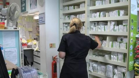 A blonde female pharmacist picking out medicine in a pharmacy