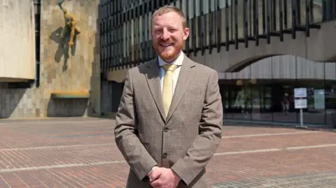 Newcastle City Council Colin Ferguson has short ginger hair and a beard. He stands outside the civic centre in Newcastle smiling.