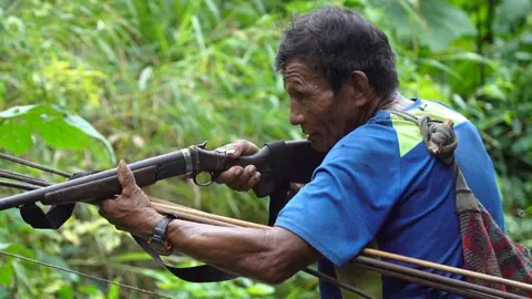 Juan in a blue T-shirt, aiming a gun 