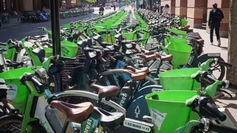 Getty Images A long row of green and teal Forest dockless e-bikes parked closely together along a city pavement.