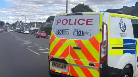 Police van in the foreground looking down a road with a police car in the distance