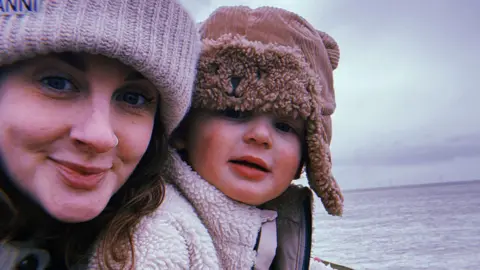 UGC Fran Barrett stands on New Brighton promenade with her son Eli . They are both  wrapped up warm and are wearing hats as they stand in front of the sea.