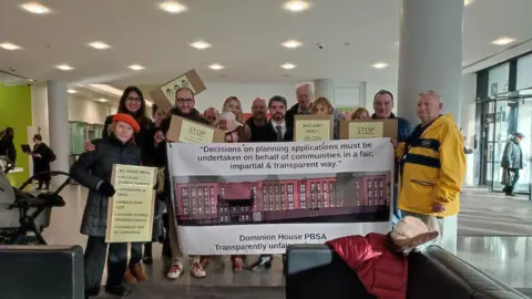 BBC A group of residents holding homepage signs and a big banner.