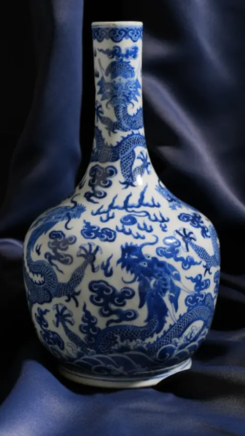 Woolley and Wallis A blue and white porcelain vase, with a very slender neck and a pattern of dragons and flower-like shapes. It is set against a backdrop of a blue shiny piece of material.