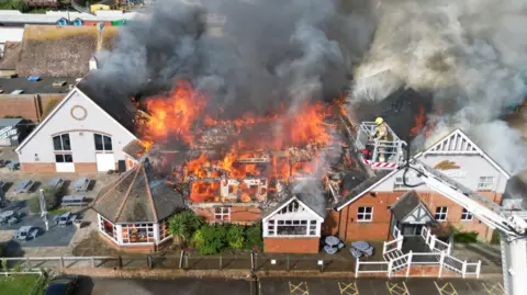 A Harvester building on fire. There is a aerial ladder platform in the foreground.